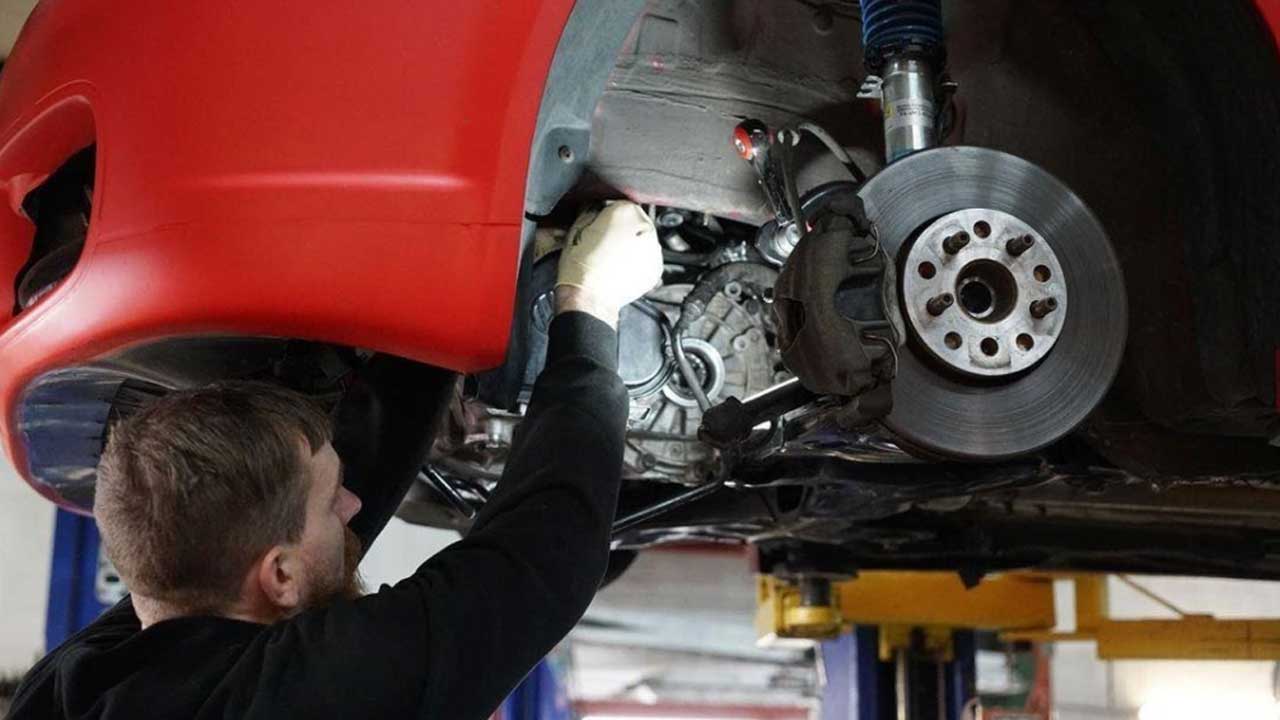 An experienced mechanic is providing transmission leak repair service to a red car at the workshop.