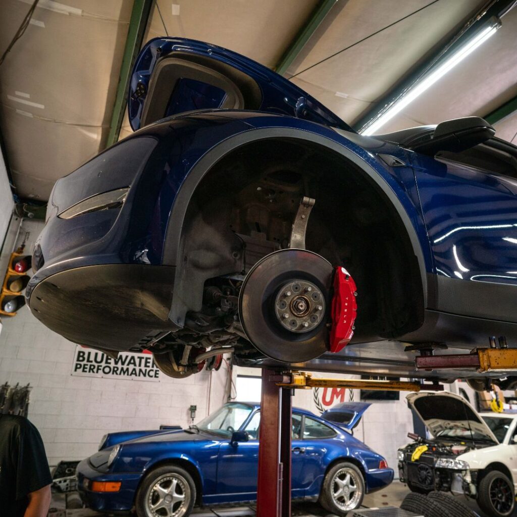 the front end of a blue sports car lifted on a hydraulic lift with no wheels and red brake calipers